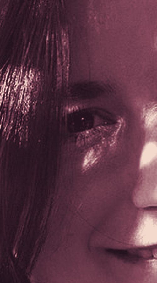 Close-up of one open eye looking at the camera, with sunlight on the cheek and dark hair beside it