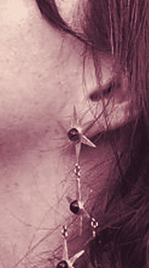 Close-up of an earlobe with a long star earring, beside the jaw and dark hair