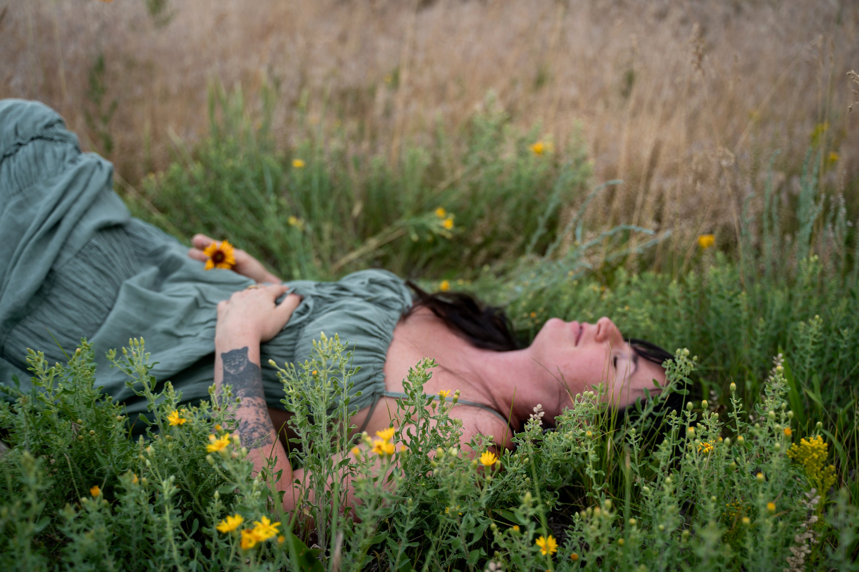 Jade Levinson, somatic intimacy coach, lying in tall golden grass in the Colorado foothills