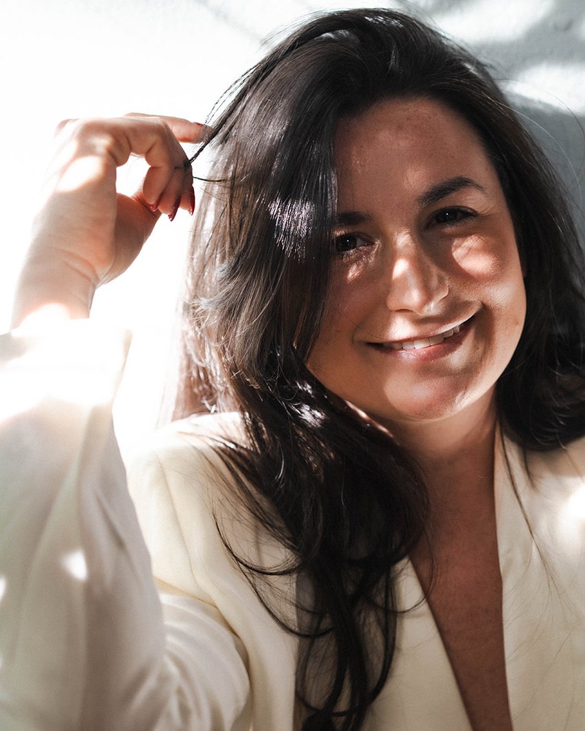 Jade Levinson, workshop facilitator and experiential designer, laughing in a white blazer in afternoon light