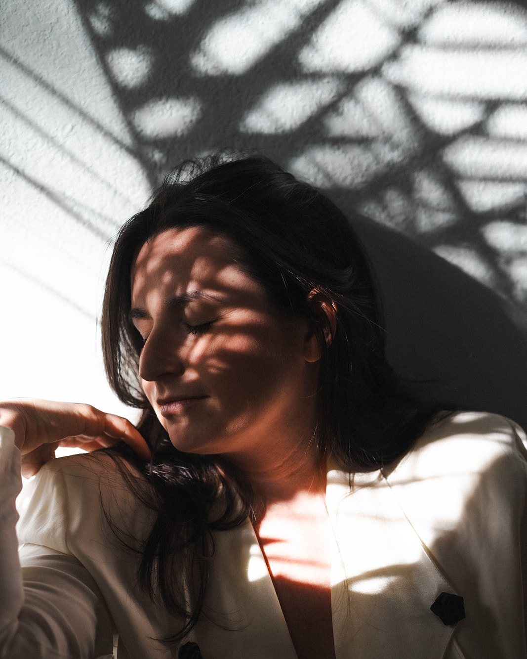 Jade Levinson in a white blazer, eyes lowered, dappled with sunlight and leaf shadows