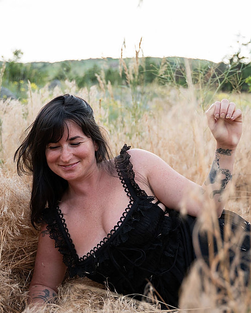 Jade Levinson, intimacy coach in Boulder, Colorado, lying back in golden meadow grass in a black dress, smiling